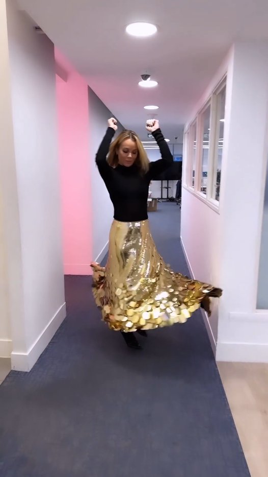 Amanda Holden dancing in an office wearing a gold sequin skirt.