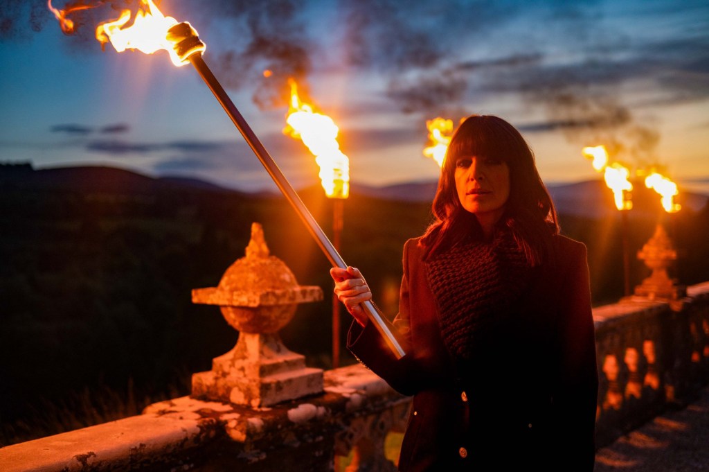 Claudia Winkleman holding a lit fire torch. 