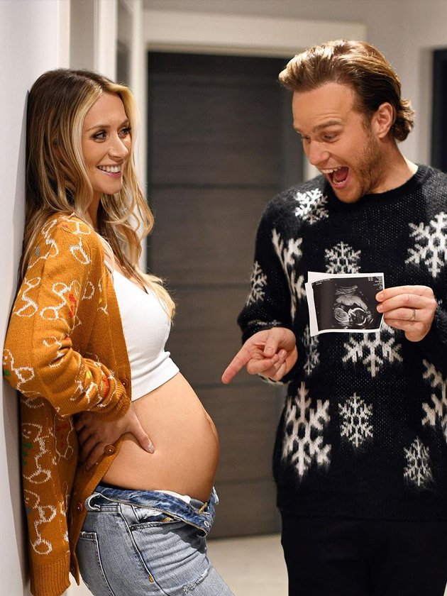 Olly Murs holding baby scan and pointing to Amelia Tank's baby bump